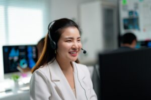 Professional Asian woman wearing headset, providing customer support while smiling at workspace